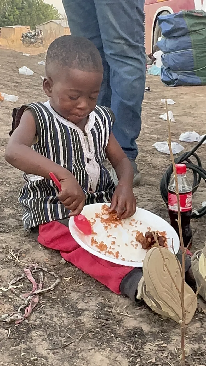 A young child eating a hot meal from a plate at a community gathering