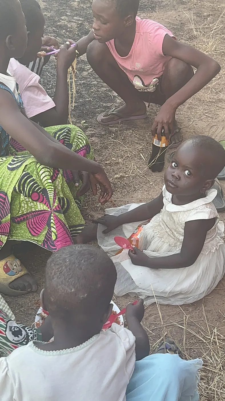 A volunteer sitting with and serving young children gathered on the ground